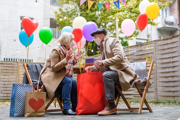 A happy senior partners in outdoor cafe in city, couple celebrating birthday. Coronavirus concept.