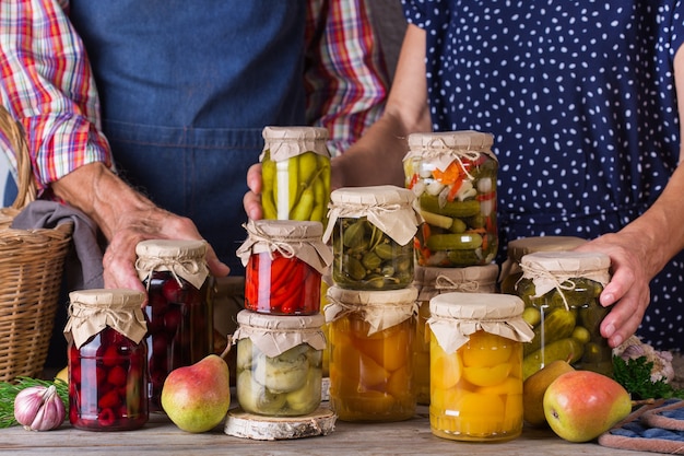 Happy senior people holding in hands jars with homemade preserved and fermented food, pickled and marinated. Harvest preservation, family time