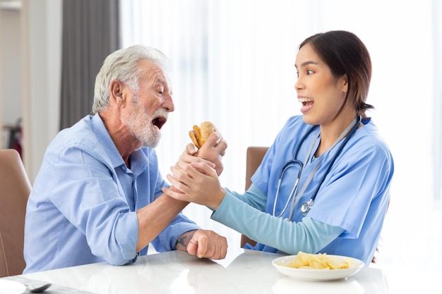 Happy senior retire adult try to eat hamburger junk food not pill from young female doctor