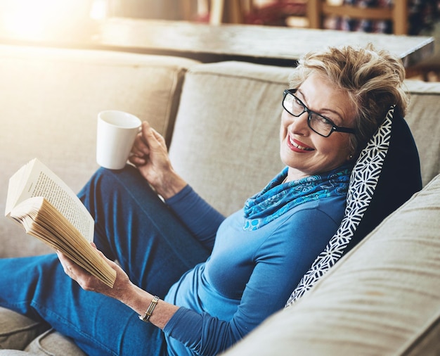 Photo happy senior woman and glasses with book story and coffee for literature in retirement home grandma novel and drink on sofa for rest relax and comfort with reading hobby for entertainment