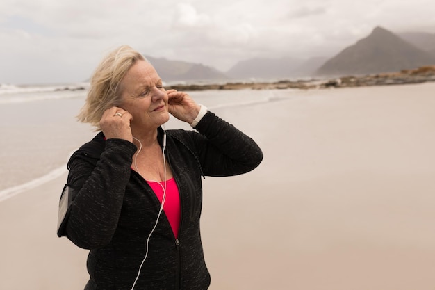 Happy senior woman listening music on earphones at the beach