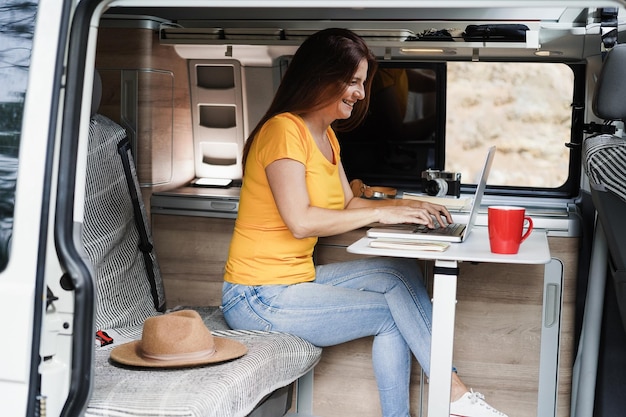 Happy senior woman using computer laptop inside camper mini van  Focus on face