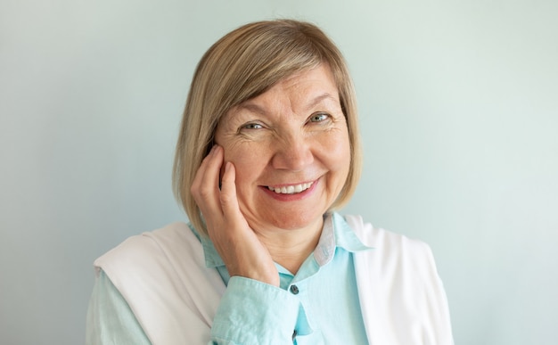 Happy senior woman with gray hair relaxing smiling is looking at the camera on a gray background