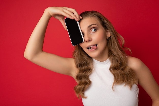 Happy sexy attractive young blonde female person wearing white t-shirt isolated on red background