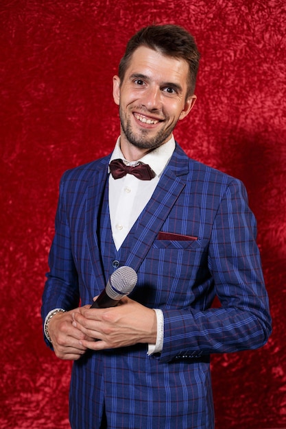 Happy showman in blue suit standing with microphone on background