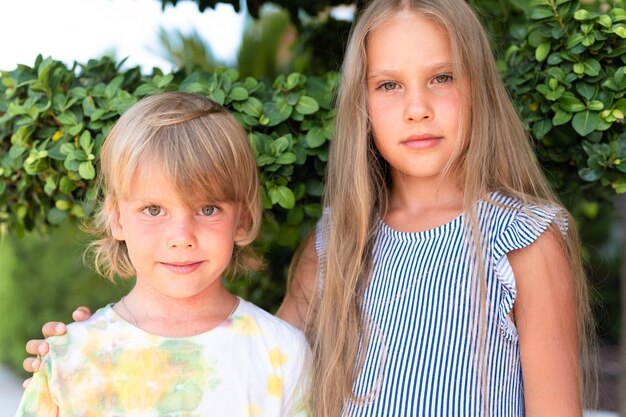 Happy sibling kids travelers boy brother of five years old and girl sister of eight years old friends hugging on green plants background and look into camera travel on nature in summer vacation