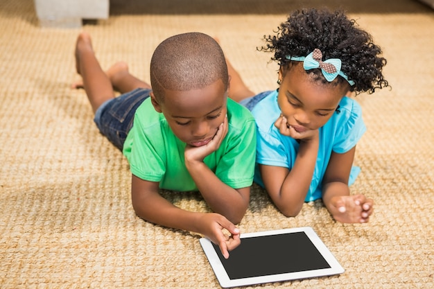 Happy siblings lying on the floor using tablet