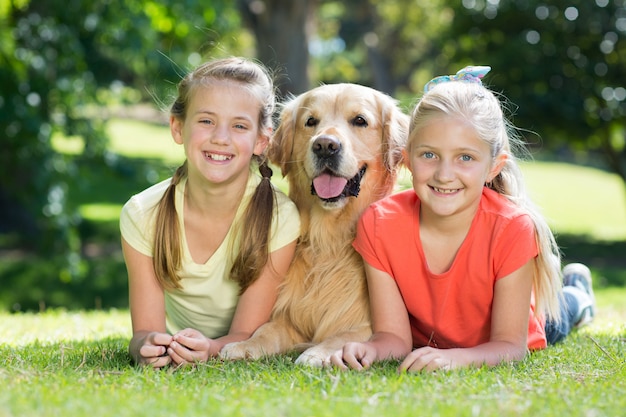 Happy sisters lying with their dog in the park 