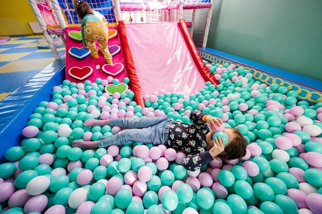 Happy sisters playing at indoor play center playground Girl lying at color balls in ball pool