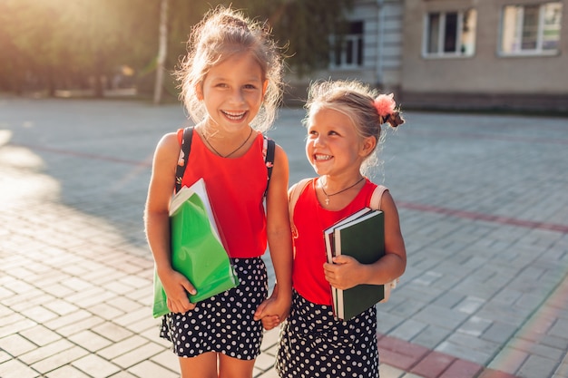 Happy sisters wearing backpacks and holding books