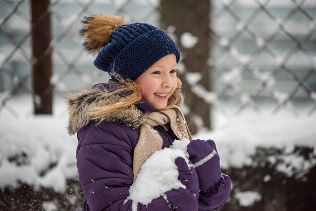 Happy small blonde girl child having fun playing with snow in winter day