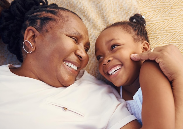 Happy smile and family of a black grandma and child in happiness relaxing and lying on a bed at home Senior African grandmother and little girl in joyful love and smiling together in the bedroom