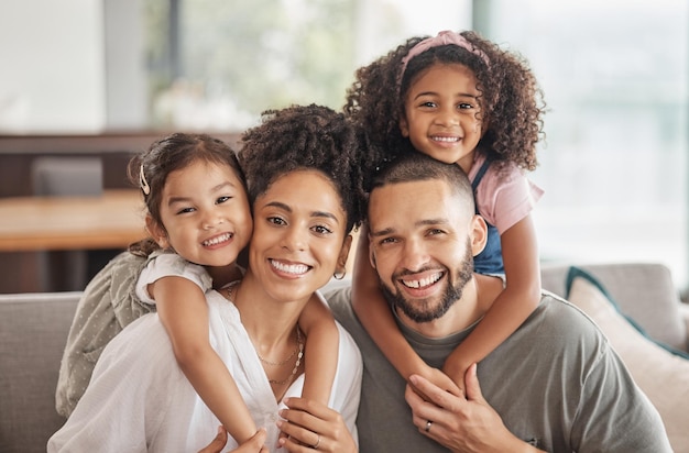 Happy smile and portrait of an interracial family sitting on a sofa in the living room at home Happiness love and adoptive parents bonding embracing and relaxing with their children in the lounge