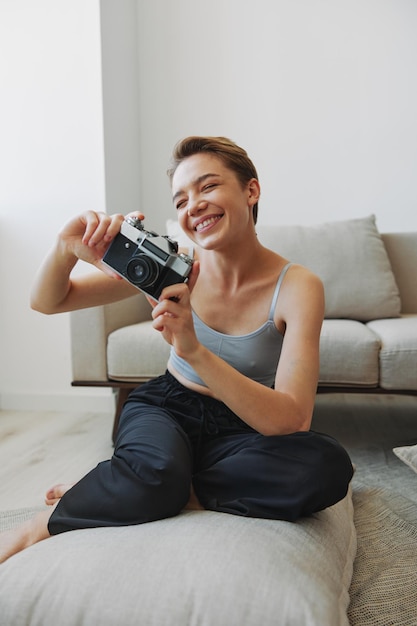 Happy smile woman holding an old camera and taking pictures of herself as a weekend photographer in home clothes with a short haircut hair without filters on a white background free copy space