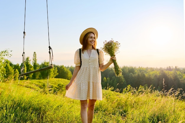 Happy smiling adult woman in dress with hat with a bouquet of wildflowers