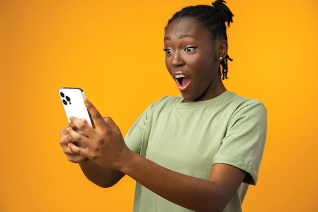 Happy smiling african american girl using her smartphone in yellow studio