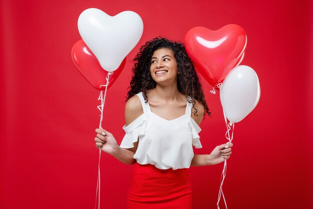 Happy smiling african girl holding colorful helium balloons isolated on red