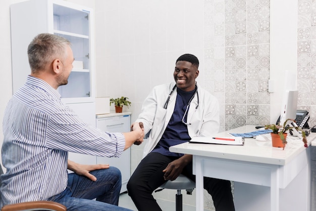 A happy smiling AfricanAmerican male doctor talks to a patient while sitting at a table