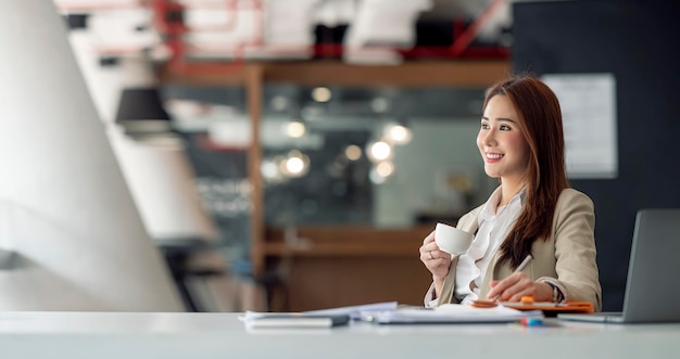 Happy smiling asian business woman working on laptop at office Businesswoman sitting at her working place