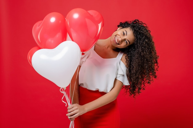 Happy smiling black woman with colorful helium balloons isolated on red