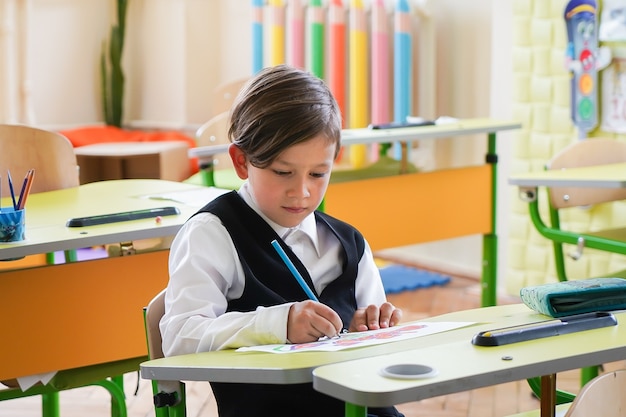 Happy smiling boy is drawing and going to school for the first time. Child with school bag and book. Kid indoors of the class room with blackboard on a background. Back to school.