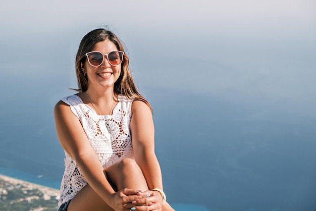 Happy smiling brunette girl on sitting in the background of the sea in sunglasses