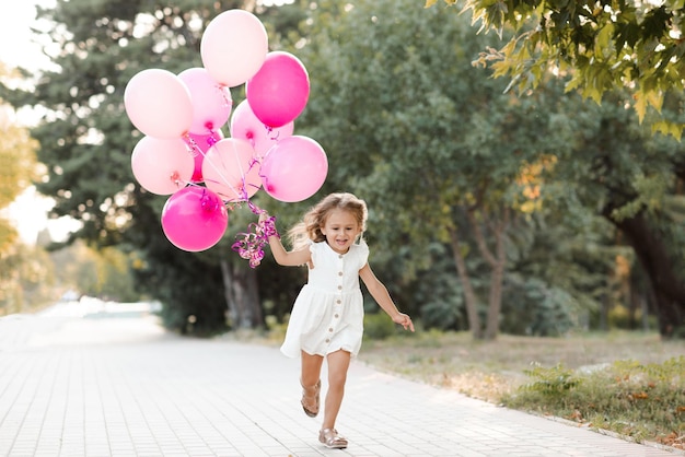 Happy smiling child girl 3-4 year old wear casual white dress holding pink baloons run cheerful