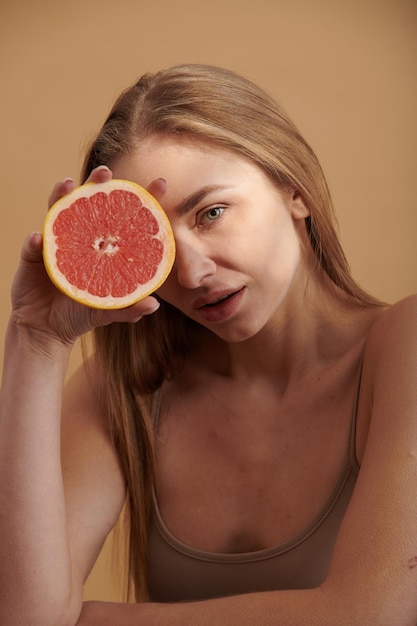 Happy smiling clean skin woman holding red grapefruit near the face