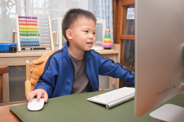 Happy smiling cute little Asian kid with personal computer making video call at home, Kindergarten boy studying online, attending school via e-learning