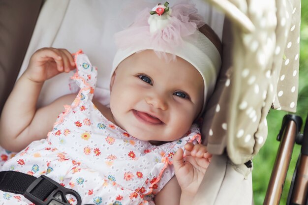 Happy smiling emotional eight-month-old blue-eyed girl sit in stroller on walk and wait for mom