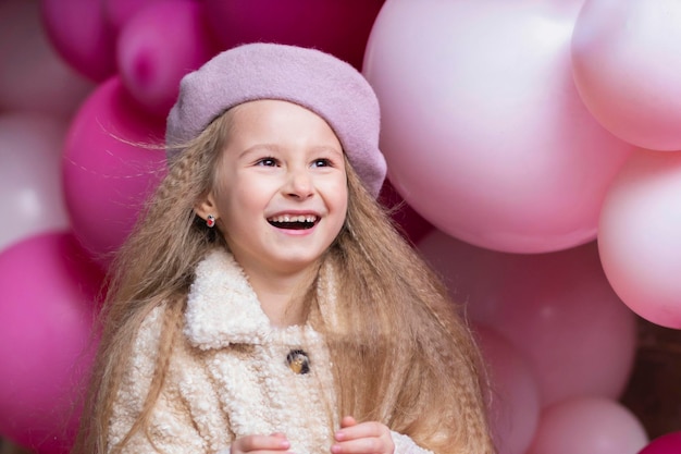 Happy smiling emotional girl in beret playing with pink, purple balloons.  Kid birthday party concept