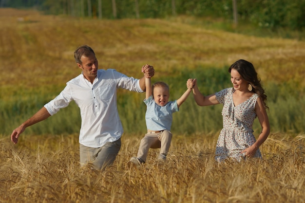 Happy smiling family walking through a wheat field. Mother, father and little boy leisures together outdoor