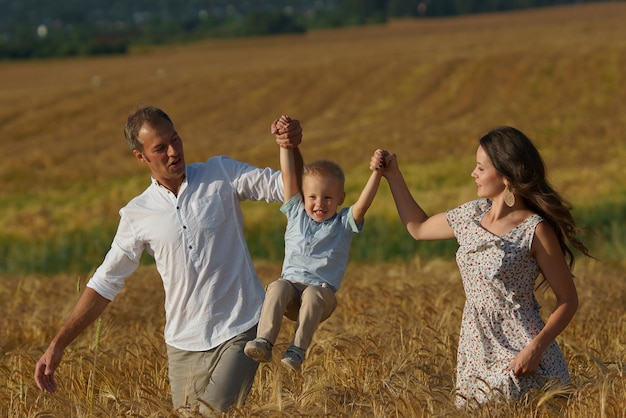 Happy smiling family walking through a wheat field. Mother, father and little boy leisures together outdoor