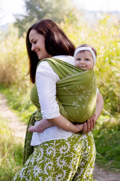 Happy smiling family with mom and girl back in green sling carrier, baby wearing