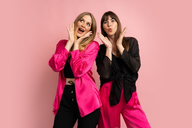 Happy smiling fashionable girls wearing stylish colorful outfit, posing on pink wall