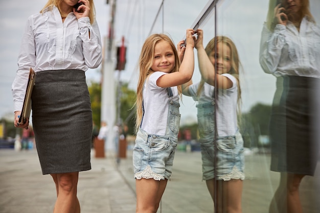 happy smiling female child looking at the photo camera while standing near the glass building