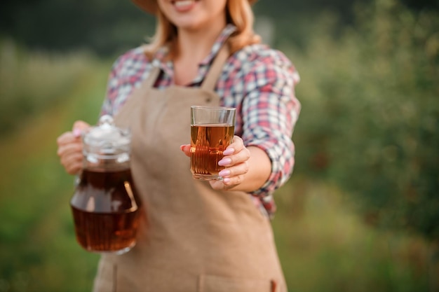 Happy smiling female farmer worker pouring tasty apple juice in glass standing in orchard garden during autumn harvest Harvesting time