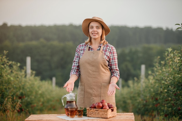 Happy smiling female farmer worker with tasty juice and fresh ripe apples in orchard garden during autumn harvest Harvesting time