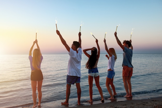 Happy smiling friends running at the beach with sparkling candles in hand