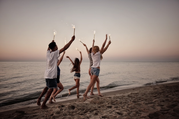 Happy smiling friends running at the beach with sparkling candles in hand