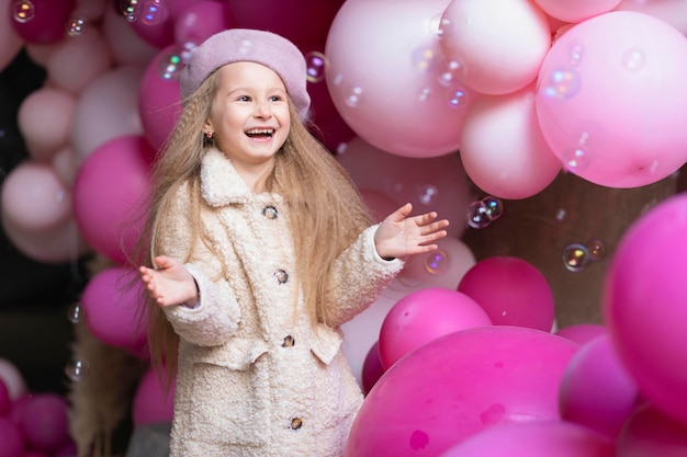 Happy smiling girl in beret playing with pink balloons, soap bubbles. Kid birthday party concept