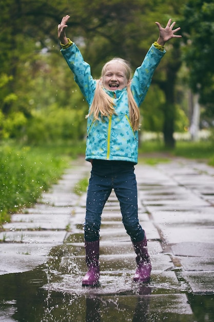 Photo happy smiling girl jumping at the puddle