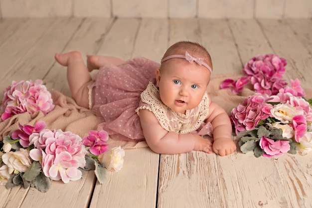 Happy smiling girl in a pink dress lies on her stomach with delicate flowers