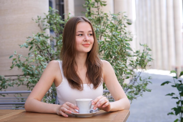 happy smiling girl young woman sitting outdoors on terrace in cafe drinking beverage tea or coffee