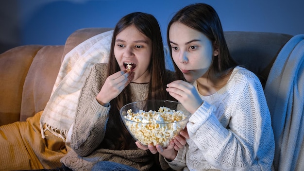 Happy smiling girls enjoying watching TV show and eating popcorn at night