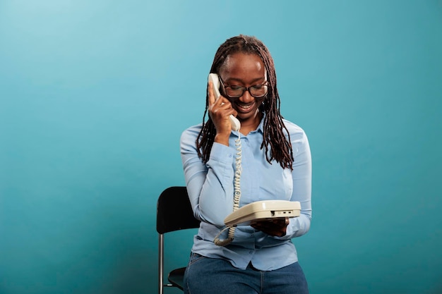 Happy smiling landline telephone operator having a conversation on wired phone on blue background. Confident positive young adult woman answering customer calling for consultancy.