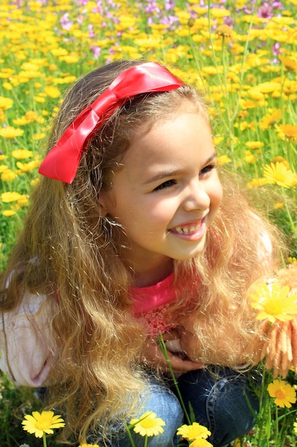 Happy smiling little girl with a red bow in her curly hair Girl on a green meadow among yellow flowers