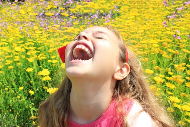 Happy smiling little girl with a red bow in her curly hair Girl on a green meadow among yellow flowers