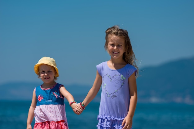 Happy smiling little sisters having fun holding their hands while walking on the beach coast during Summer vacation  Healthy childhood lifestyle concept