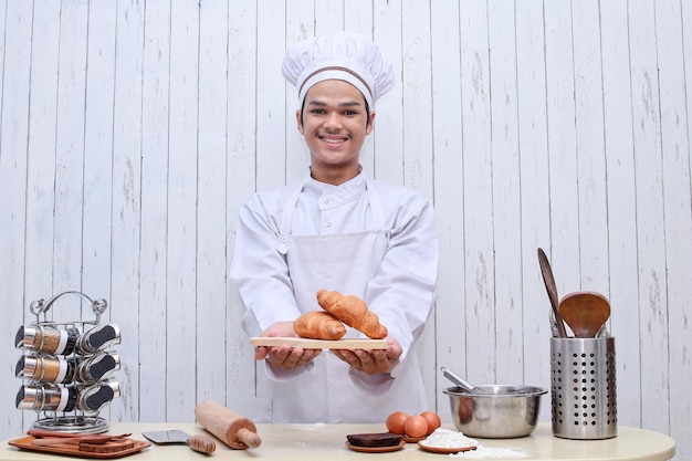 Happy smiling male chef or baker in toque and apron holding a plate of croissants